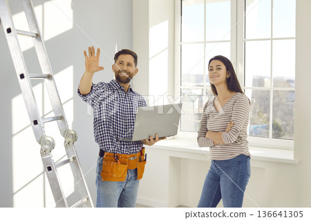 Happy worker with laptop talking to young woman about repairs and renovations in her house 136641305