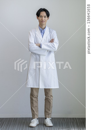 A man in his 30s in a white coat with his arms crossed, smiling at the camera, full body, white background, portrait A man in his 30s in a white coat with his arms crossed, smiling at the camera, full body, white background, portrait 136641658