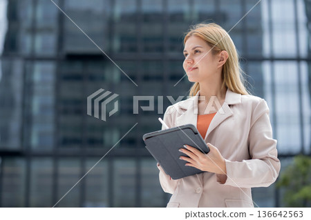 Young caucasian businesswoman writing on digital tablet in city. Young caucasian businesswoman writing on digital tablet in city. 136642563