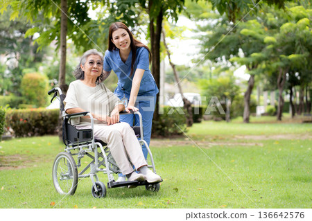 Young caucasian nurse comforting with patient while sitting on wheelchair in outdoor park. 136642576