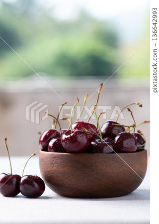 Fresh red cherries with water droplets in a wooden bowl with green nature background Fresh red cherries with water droplets in a wooden bowl with green nature background 136642993