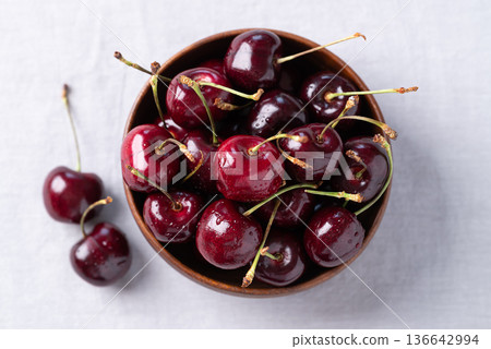 Top view of fresh red cherries with water droplets in a wooden bowl on fabric background 136642994