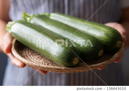 Close up of hands holding a basket of green zucchini harvested from a farm 136643010