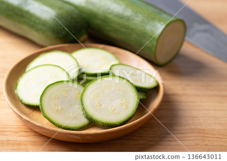 Slices of fresh green zucchini in a wooden plate, ready for healthy cooking Slices of fresh green zucchini in a wooden plate, ready for healthy cooking 136643011