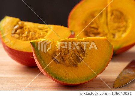 Sliced orange Kuri squash (Hokkaido pumpkin) on a wooden cutting board with a knife Sliced orange Kuri squash (Hokkaido pumpkin) on a wooden cutting board with a knife 136643021