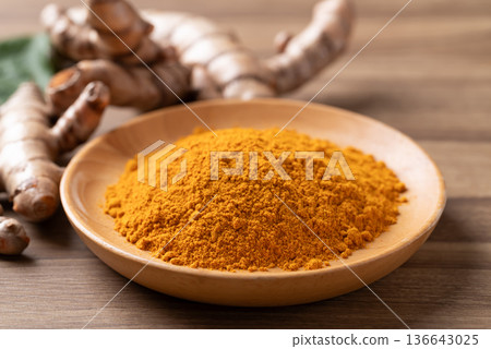 Turmeric powder in a wooden bowl with fresh roots on a wooden background. Organic healthy spice Turmeric powder in a wooden bowl with fresh roots on a wooden background. Organic healthy spice 136643025