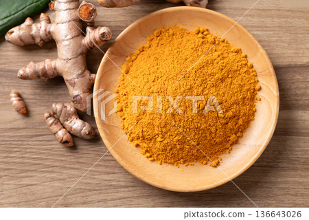 Turmeric powder in a wooden bowl with fresh roots on a wooden background. Organic healthy spice Turmeric powder in a wooden bowl with fresh roots on a wooden background. Organic healthy spice 136643026