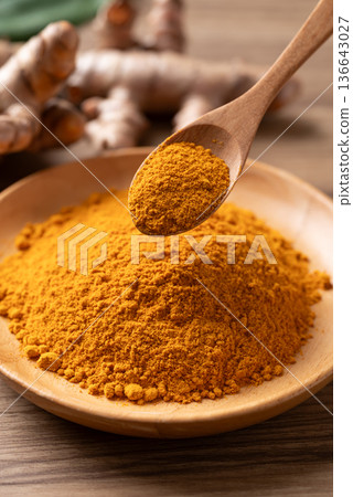 Turmeric powder in a wooden bowl with a wooden spoon scooping it Turmeric powder in a wooden bowl with a wooden spoon scooping it 136643027