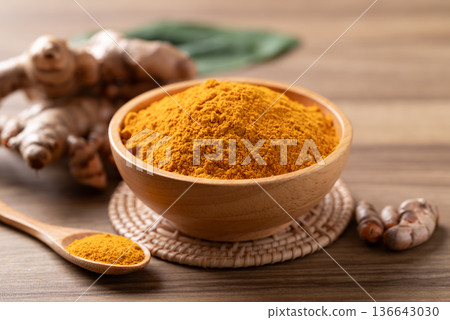 Turmeric powder in a wooden bowl with a wooden spoon and fresh turmeric roots on a wooden background Turmeric powder in a wooden bowl with a wooden spoon and fresh turmeric roots on a wooden background 136643030