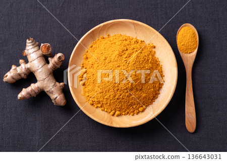 Turmeric powder in a wooden bowl with a wooden spoon and fresh turmeric roots on black background Turmeric powder in a wooden bowl with a wooden spoon and fresh turmeric roots on black background 136643031