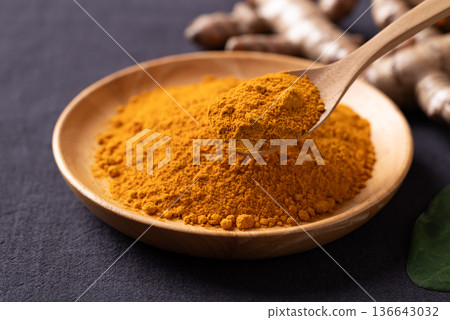 Turmeric powder in a wooden bowl with a wooden spoon scooping it Turmeric powder in a wooden bowl with a wooden spoon scooping it 136643032