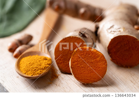 Fresh turmeric roots and turmeric powder in a wooden apoon on a wooden board. Organic healthy spice Fresh turmeric roots and turmeric powder in a wooden apoon on a wooden board. Organic healthy spice 136643034
