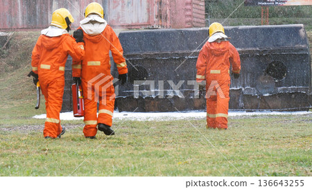 Firefighter Rescue team training in fire fighting extinguisher. Firefighter teamwork fighting with flame using fire hose chemical water foam spray engine. Fireman wear hard hat, safety suit uniform Firefighter Rescue team training in fire fighting extinguisher. Firefighter teamwork fighting with flame using fire hose chemical water foam spray engine. Fireman wear hard hat, safety suit uniform 136643255