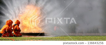 Firefighter Rescue training in fire fighting extinguisher. Firefighter fighting with flame using fire hose chemical water foam spray engine. Fireman wear hard hat, safety suit uniform for protection 136643256