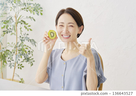 一位女士在客廳拿著獼猴桃，豎起大拇指。 136643527