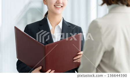 Young woman/businesswoman talking while holding a file Young woman/businesswoman talking while holding a file 136644390