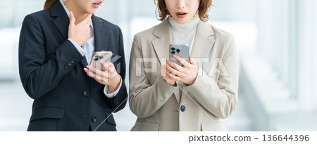 Two women/businesswomen surprised at their smartphones 136644396