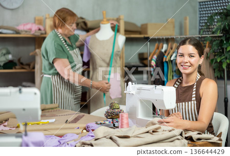 Young woman sews on machine female assistant sews on mannequin Young woman sews on machine female assistant sews on mannequin 136644429