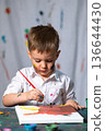 一個自由奔放的男孩正在畫畫，顏料濺到了他的衣服和牆上。 136644430