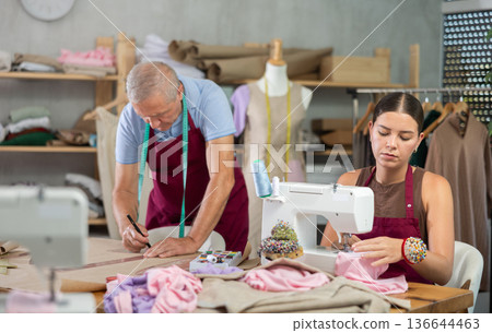 Young woman sewing male assistant drawing pattern on paper Young woman sewing male assistant drawing pattern on paper 136644463