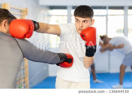 Man and guy in boxing gloves punch deliver blow each other during training sparring session. Man and guy in boxing gloves punch deliver blow each other during training sparring session. 136644530