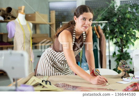 Female fashion designer drawing on paper with curved rulers in workshop 136644580