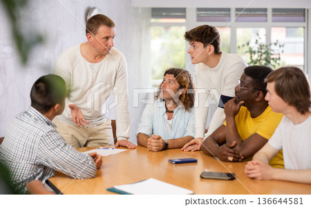 Middle-aged man instructor explaining the topic to group of guys around the table Middle-aged man instructor explaining the topic to group of guys around the table 136644581