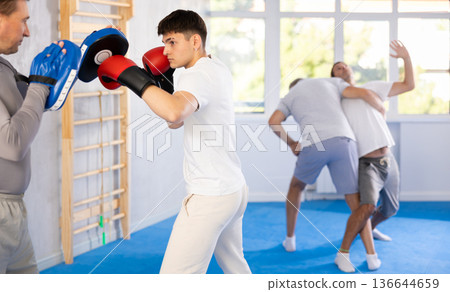 Guy in boxing training practices punches with man in mitts in sport club Guy in boxing training practices punches with man in mitts in sport club 136644659