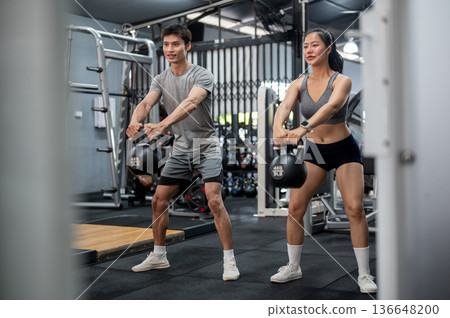 Fitness trainer coach man teaching and holding kettlebell exercising with asian woman client in gym. 136648200