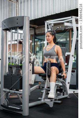 Pretty asian woman client in sportswear sitting and exercising with a weight lift equipment in gym. 136648218