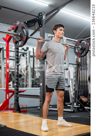 Asian man client in sportswear standing and exercising with barbell weight lifting equipment in gym. Asian man client in sportswear standing and exercising with barbell weight lifting equipment in gym. 136648219