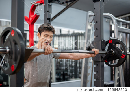 Asian man client in sportswear standing and holding barbell equipment to do weight lifting in gym. 136648220