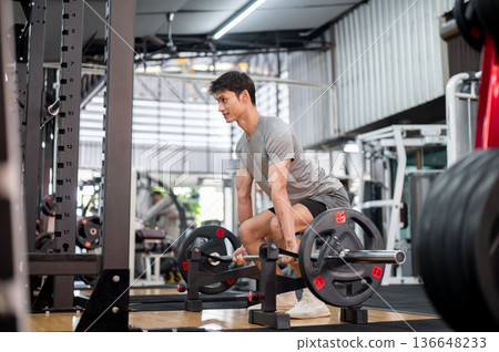 Asian man client in sportswear crouching down holding barbell exercising by doing weight lift in gym 136648233