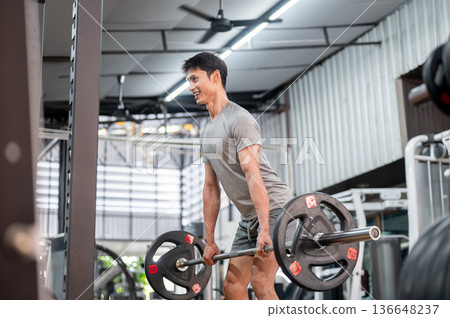 Happy asian man client in sportswear standing holding barbell exercising doing weight lifting in gym Happy asian man client in sportswear standing holding barbell exercising doing weight lifting in gym 136648237