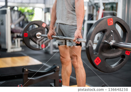 Close up of man client in sportswear standing holding barbell exercising doing weight lifting in gym Close up of man client in sportswear standing holding barbell exercising doing weight lifting in gym 136648238