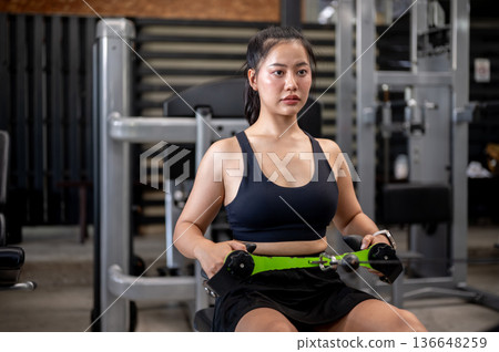 Asian woman fitness trainer or a client sitting exercising with stretching equipment machine in gym. Asian woman fitness trainer or a client sitting exercising with stretching equipment machine in gym. 136648259