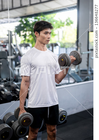 Asian man fitness trainer coach or client standing holding dumbbells in both hands exercising in gym 136648277