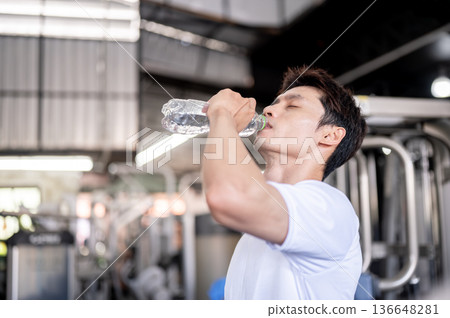 Asian man client or fitness trainer coach holding bottle drinking water after exercising in the gym. 136648281