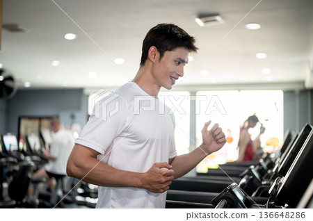Handsome asian man client or a fitness trainer coach exercising by running on treadmill in the gym. Handsome asian man client or a fitness trainer coach exercising by running on treadmill in the gym. 136648286