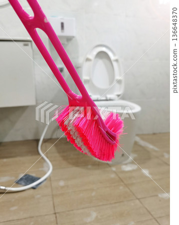 A pink and white toilet brush against a blurred bathroom interior background. A pink and white toilet brush against a blurred bathroom interior background. 136648370