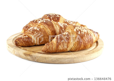 Three golden croissants with pearl sugar on a round wooden board isolated on white background Three golden croissants with pearl sugar on a round wooden board isolated on white background 136648476