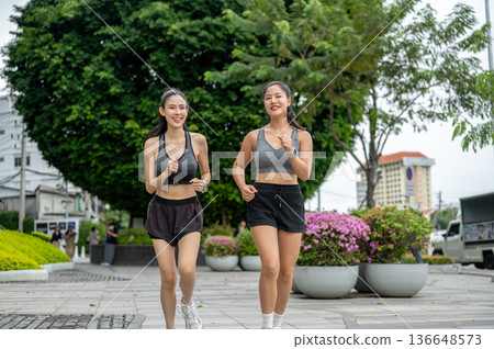 Asian woman friends in sportswear exercising by running or jogging on pavement in mall's garden park 136648573