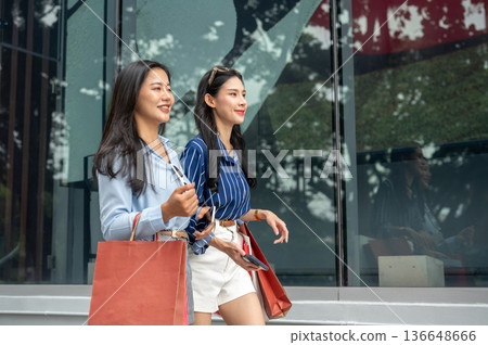 Pretty asian woman and friend carrying shopping bags while walking together outside a shopping mall. Pretty asian woman and friend carrying shopping bags while walking together outside a shopping mall. 136648666