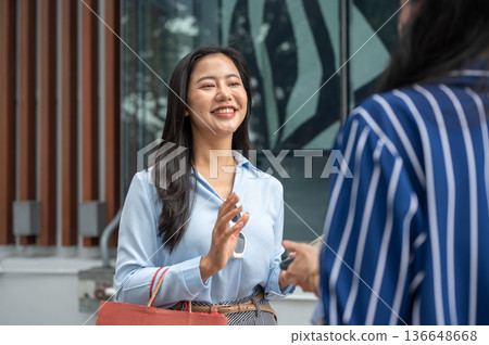 Pretty asian woman carrying shopping bag talking to a friend while standing outside a shopping mall. Pretty asian woman carrying shopping bag talking to a friend while standing outside a shopping mall. 136648668