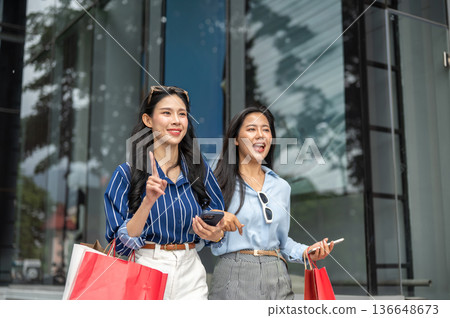 Pretty asian woman and friend carrying shopping bag talking walking together outside a shopping mall Pretty asian woman and friend carrying shopping bag talking walking together outside a shopping mall 136648673