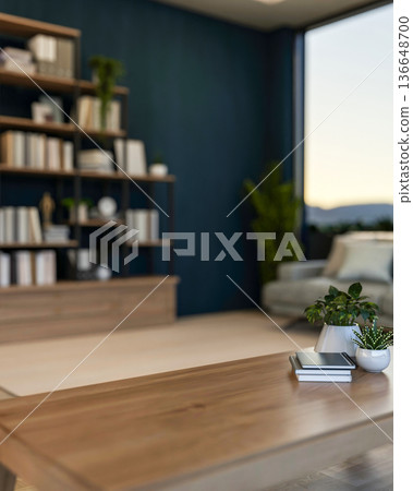 Books and potted plant on wooden table across bookshelf and sofa aside window wall in dark blue room 136648700