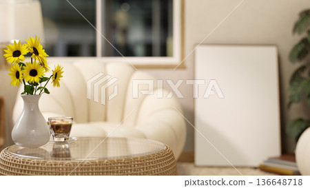Sunflower vase and coffee cup on glass table across sofa and canvas frame on floor in a living room 136648718