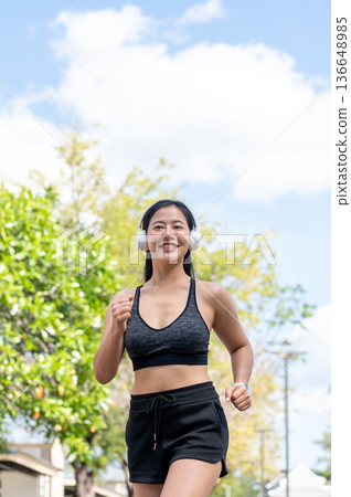 Asian woman in sportswear listening to music in headphone and running jogging exercise in sunny park Asian woman in sportswear listening to music in headphone and running jogging exercise in sunny park 136648985