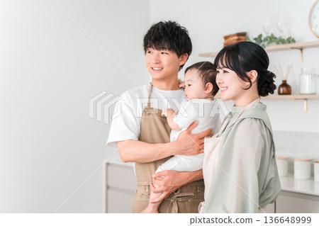 一對穿著圍裙的夫婦抱著嬰兒在廚房裡,一家人 一對穿著圍裙的夫婦抱著嬰兒在廚房裡,一家人 136648999
