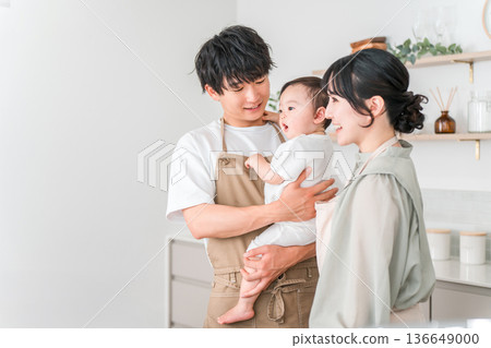 一對穿著圍裙的夫婦抱著嬰兒在廚房裡,一家人 一對穿著圍裙的夫婦抱著嬰兒在廚房裡,一家人 136649000